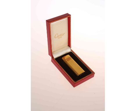 A CARTIER YELLOW METAL LIGHTER, the reeded case with rounded sides, in a Cartier box. 7cm