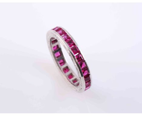 A RUBY ETERNITY RING, the twenty seven square cut rubies all channel set to the entirety of the band between engraved detaili