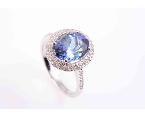 A TANZANITE AND DIAMOND RING, the oval cut tanzanite four claw set within an inner and outer stepped surround set to the enti