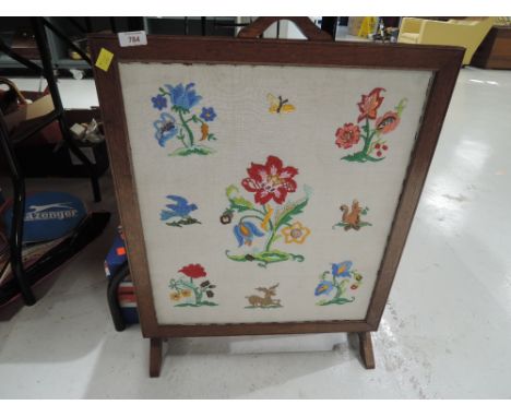An embroidered fire screen in an oak frame