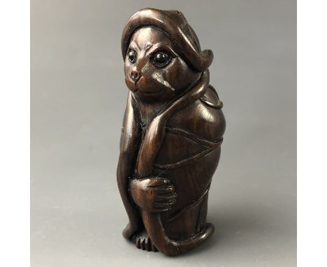 A Japanese carved wood netsuke modelled as a cat-like animal wrapped in a lily pad 