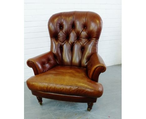 A brown leather button back armchair, on turned supports and brass caps and castors, 104 x 82cm 