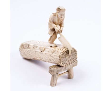 A Japanese ivory okimono of a carpenter late Meiji standing upon and sawing a tree trunk raised and supported on a single tre