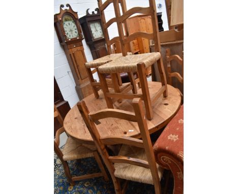 A rustic pine circular dining table and set of six ladderback chairs having rush seats