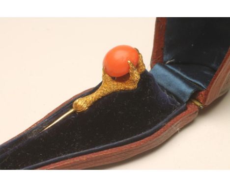 A MID VICTORIAN STICK PIN, the polished coral bead held in the claws of an eagle with chased scales, claw 1 1/4" long overall