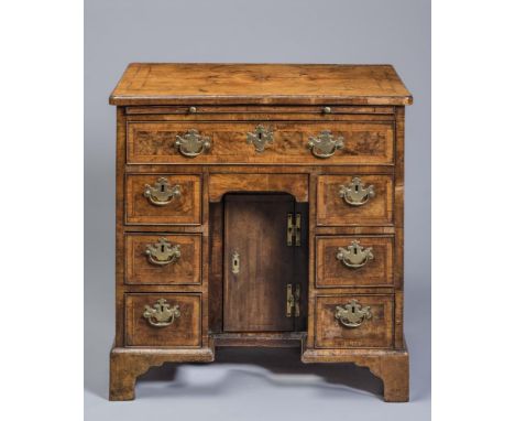 AN EARLY GEORGIAN SMALL WALNUT KNEEHOLE DESK, the rounded oblong top quarter veneered with feather banding, slide below over 