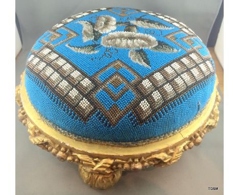 A Victorian carved & gilt foot stool with bead work top. 29 cm diameter