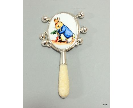 A silver babies rattle with enamel plaque depicting peter rabbit and bone handle