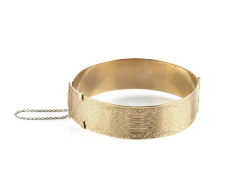A yellow precious metal bangle, of hinged oval form, the frontispiece with engine-turned decoration, stamped 'ACC 9CT', inner
