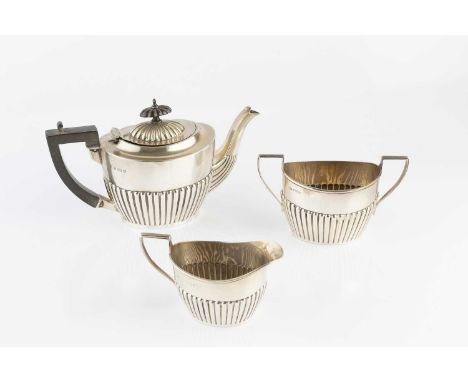 An Edwardian silver three piece bachelor's tea service, with half lobed decoration, the tea pot with ebonised handle and knop