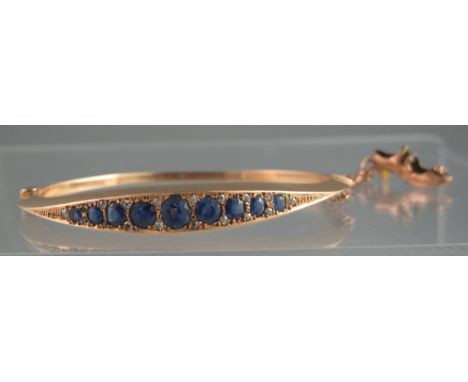AN EARLY 20TH CENTURY 15CT GOLD, SAPPHIRE AND DIAMOND HINGED BANGLE.  The nine sapphires graduated from the centre and separa
