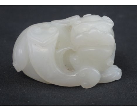 SMALL CHINESE WHITE JADE CARVED HARDSTONE FIGURE of a recumbent temple lion holding stylized ruyi sceptre by ribbon in his mo