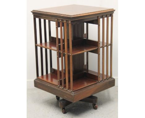 EARLY 20TH CENTURY MAHOGANY SQUARE REVOLVING BOOKCASE with vertically slatted sides and fitted shelves on a cruciform base wi