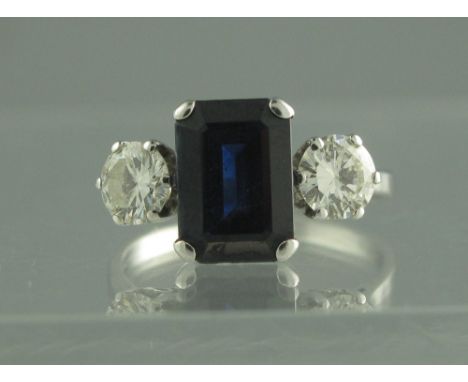 AN 18CT WHITE GOLD, SAPPHIRE AND DIAMOND THREE STONE RING. The step cut sapphire measures 10 x 7mm. Set to either side with a