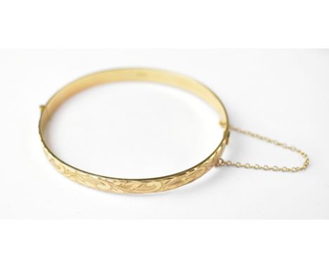 A 9ct gold hinged bangle, half decorated with scrolls and leaves, with push clasp and gold safety chain, internal diameter fr