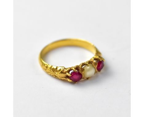 A yellow metal ruby and pearl ring, the centred claw set pearl flanked by two cut rubies, chased detail to the shoulders, on 