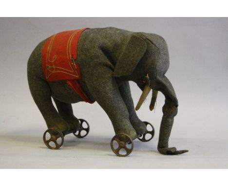 A STEIFF ELEPHANT ON WHEELS, grey felt, white felt tusks, missing one eye, other eye damaged, red felt blanket with gold thre