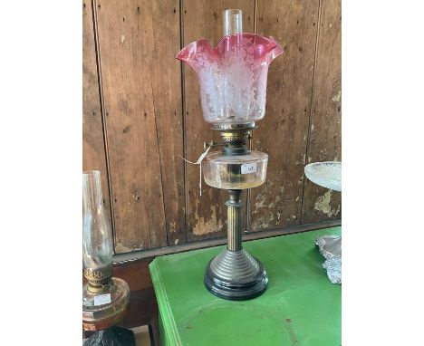 A late Victorian oil lamp with cranberry and clear glass shade, etched with floral detail above the clear glass reservoir wit