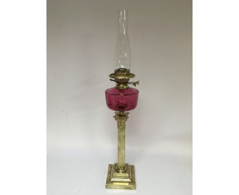 A brass oil lamp with a cranberry glass reservoir and raised on a Corinthian column, approx height 81cm.