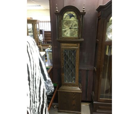 A smaller modern oak longcase clock with visible pendulum and rotating dial, approx 196cm.