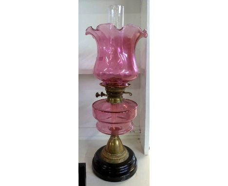 Oil lamp with cranberry tinted frilled shade over a cranberry font and brass base, total height approx 58cm