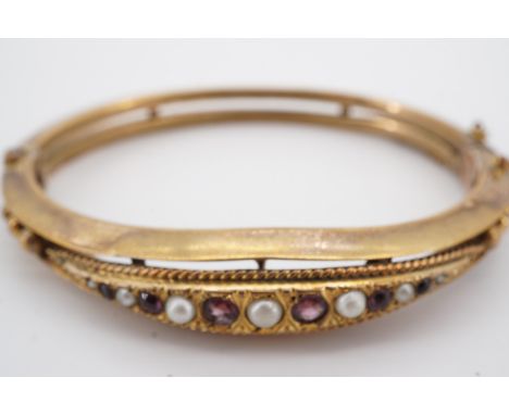 A Victorian rolled gold hinged bangle set with graduated pearls and amethyst coloured stones