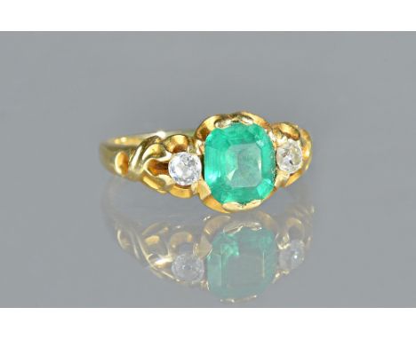 A gold, emerald and diamond set three stone ring, mounted with the step cut emerald at the centre, between two cushion shaped