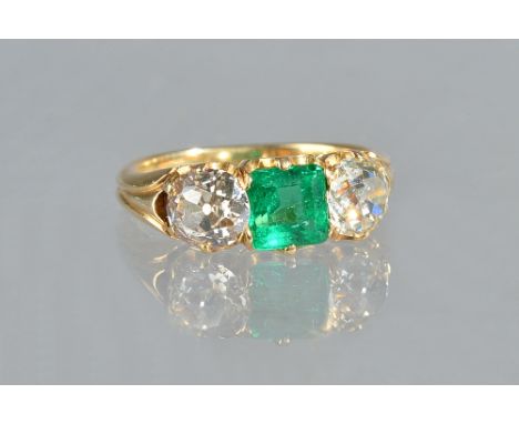 A gold, emerald and diamond set three stone ring, claw set with a square step cut emerald to the centre, between two cushion 