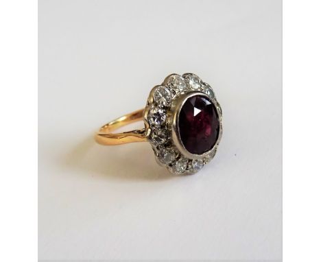 A gold, ruby and diamond set oval cluster ring, collet set with the oval cut ruby at the centre, in a surround of twelve circ