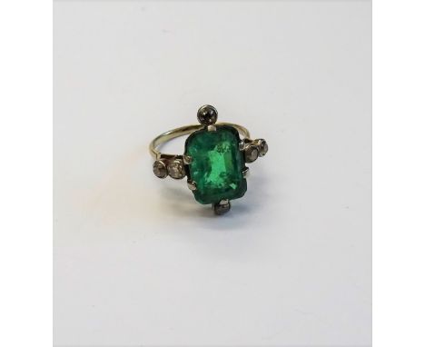 An emerald and diamond ring, claw set with the cut cornered rectangular step cut emerald to the centre, between two pairs of 