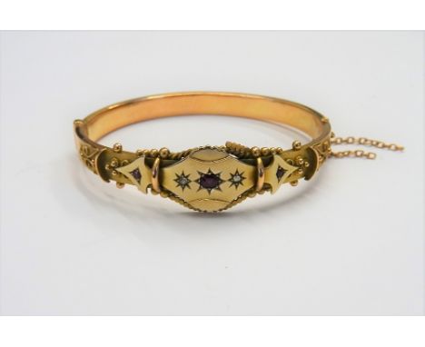 A 9ct gold, ruby and rose diamond set oval hinged bangle, star set with the principal cushion shaped ruby at the centre, betw