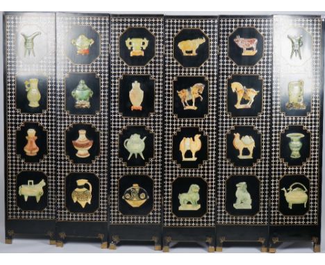 A mid-20th century Eastern black lacquer six fold screen, relief decorated with soapstone vessels, animals and mother-of-pear