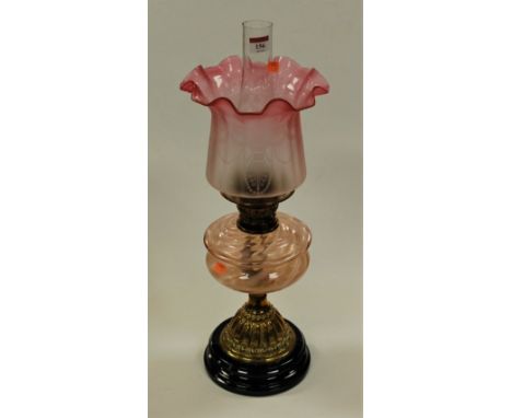 A Victorian pedestal oil lamp having cranberry tinted etched frilled glass shade above a pink tinted glass font on a brass pe