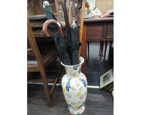 A ceramic floor vase used as a stick stand with walking sticks and umbrellas