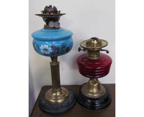 A Victorian oil lamp with a cranberry glass reservoir together with another with a blue glass reservoir painted with flowers