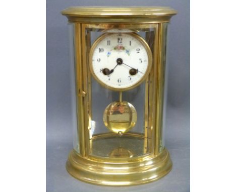 A brass cased mantel clock with four bevelled and curved glass panels, the Arabic dial in ivory colour with floral and foliat