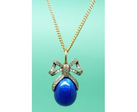 A 14ct gold pendant with a blue guilloche enamel egg and clear stones set in a bow shape. 