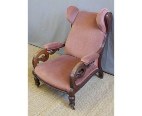 A Victorian mahogany wing back chair with scrolling pierced arms, turned front legs and sabre back legs raised on ceramic cas