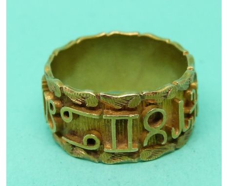 A yellow metal ring with symbols/ letters around the band and a foliate border 