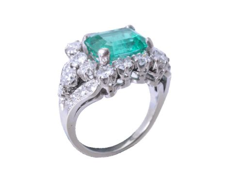 ΩAn emerald and diamond cluster ring, the step cut emerald with canted corners, estimated to weigh 3.15 carats total, within 