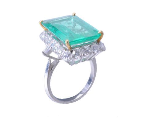 An emerald and diamond cluster ring, the step cut emerald with canted corners estimated to weigh 9.20 carats, within a surrou