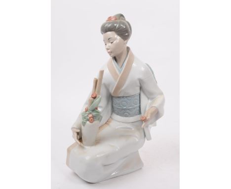 NAO, Spain - A large hand painted fine bone china porcelain figure of kneeling geisha. The figure depicting the geisha holdin
