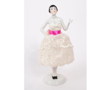 An early 20th century porcelain china pin / half doll. Having a three layer pierced dress, pin ribbon on a circular base with