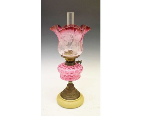 Early 20th Century cranberry and vaseline oil lamp with engraved shade, the cast metal pedestal base raised on ceramic foot, 