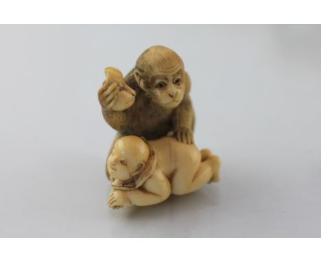 A Japanese carved ivory netsuke, Meiji period (1868-1912) finely carved as a monkey holding a mask aloft, a baby crawling in 