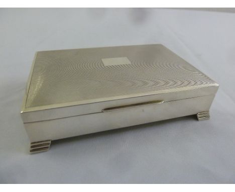 A rectangular silver engine turned cigarette box with hinged cover on four stepped feet