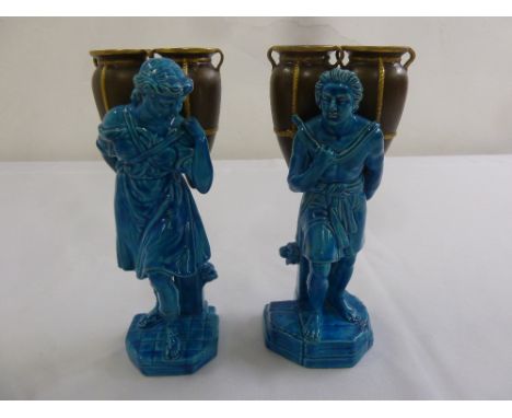 A pair of continental ceramic blue ground figurines of a lady and man carrying urns on shaped square bases
