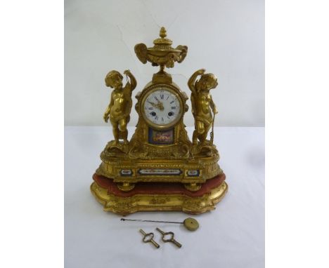 A French gilded metal mantle clock with putti figurines, Sevres style panels, enamel dial with Roman numerals, to include sta