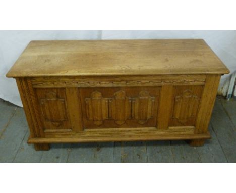 A rectangular blonde oak blanket box with carved panel sides, hinged cover on four bracket feet