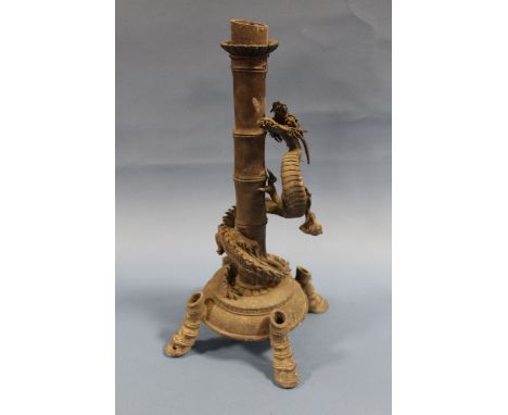 A CHINESE BRONZED TABLE CANDLESTICK, modelled as a coiled dragon around a bamboo stem, raised on four hoof type feet, H 37 cm